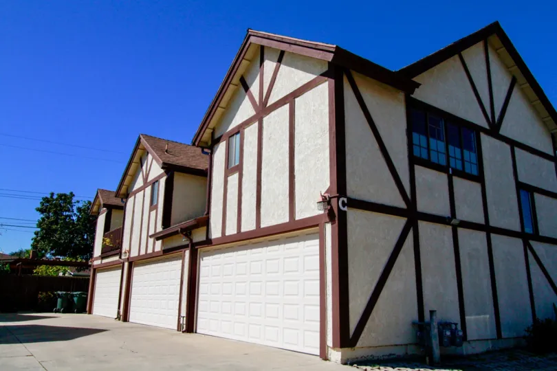Row of white stucco two-story units with brown accenting and dual garages at Picadilly Terrace in Costa Mesa, CA
