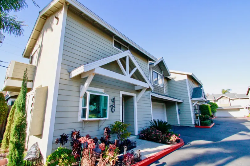 THE LIGHT WHITE COLOUR BUILDING AND A BEAUTIFUL WINDOW AT IT HAS A SMALL FLOWER WASH AND SOME PLANTS WITH FLOWERS NEAR TO THE HOUSE AND TREES ALSO BEHIND THE HOUSE.