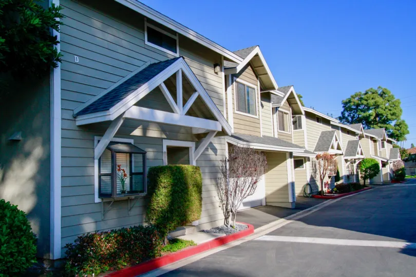 A row of town homes with topiary bushes out front on a sunny day in Quiet Bay Townhomes, Costa Mesa, Ca.
