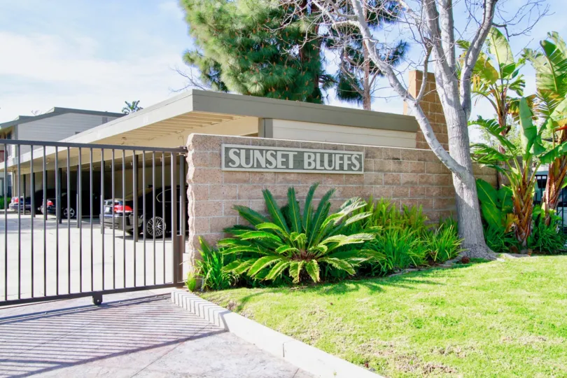 Sunset Bluffs gate with trees and bushes on a sunny day.