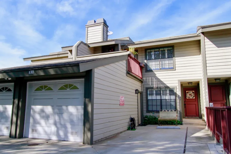 A tan two story residence with a red door and balcony on a sunny day, at Sunset Bluffs in Costa Mesa, Ca.