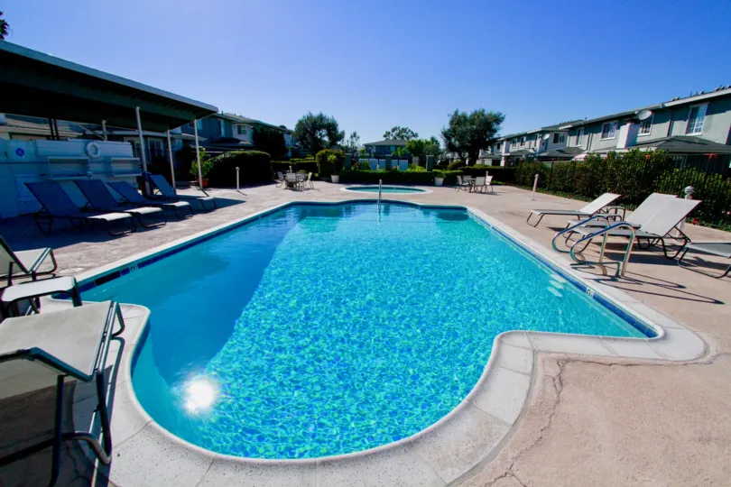 THE SWIMMING POOL LOCATED WITH SITTING CHAIRS AND SUN REFLECTS ON THE POOL SOME TREES ARE NEAR TO THE POOL AND LOOKING BEAUTIFUL.
