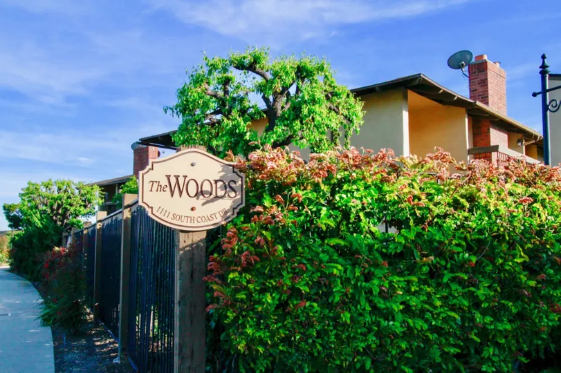 THE PLANTS WITH FLOWERS LOOKING BEAUTIFUL AND A SIGN BOARD NEAR TO THE PLANTS AND A HOUSE WITH DISH LOCATED INSIDE THE GATE AND SOME TREES NEAR TO THE ENTRANCE GATE.