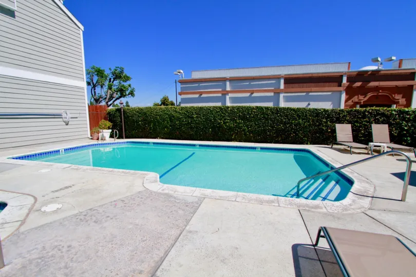 A oddly shaped crystal blue pool with steps and railing at Victoria Garden Villas in Costa Mesa CA