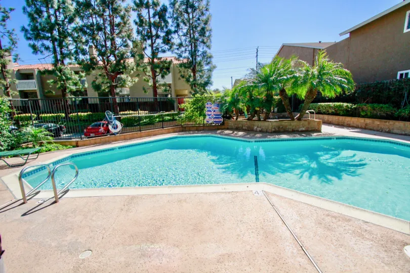 THE SWIMMING POOL WITH A CAR PARKING AND A SIGN BOARD SOME TREES AND PLANTS ALSO AVAILABLE AT THE MORNING TIME AND A BUILDING ALSO NEAR TO THE POOL