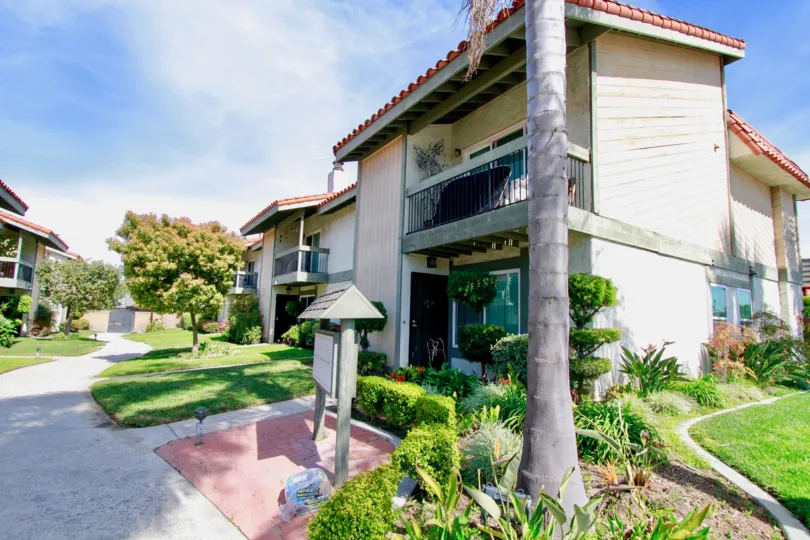 A BUILDING WITH TWO FLOORS AND ALSO A BALCONY ALSO LOCATED AT THE FIRST FLOOR AND SOME GRASS AND PLANTS IN FRONT OF THE HOUSE A TREE ALSO THERE
