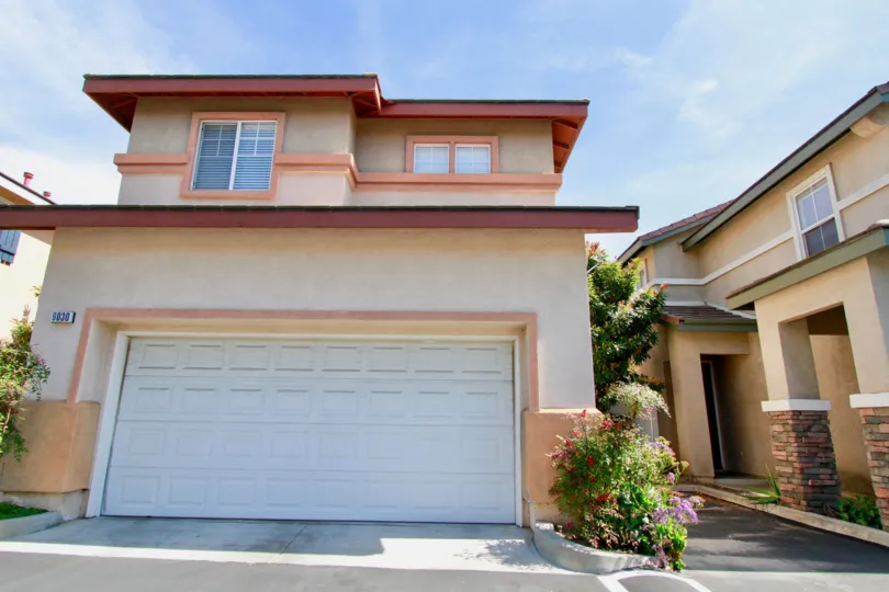 A small two story family home with two car garage. Neighboring homes are in close proximity and walkway between houses leads to the front door.