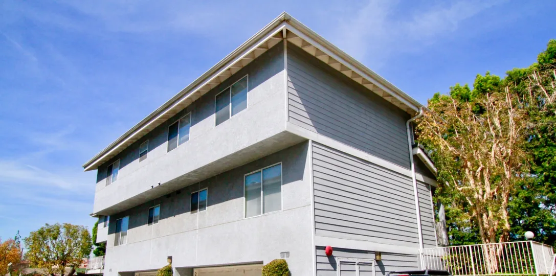 Three story building with four windows on the upper two levels located in front of large trees