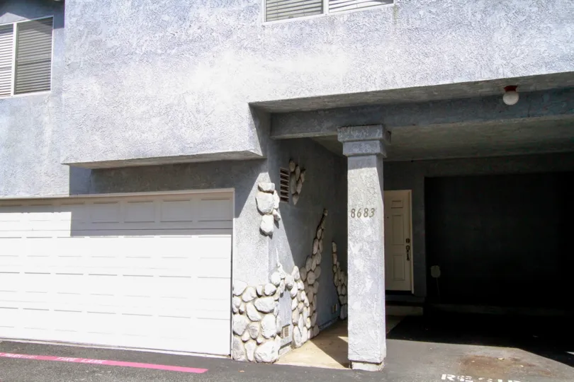 A BUILDING DIFFERENT DESIGN WALL AND LOOKS CEMENT COLOR AND A LAMP ALSO AT THE TOP AND A DOOR WITH SANDAL COLOR ALSO CLOSED