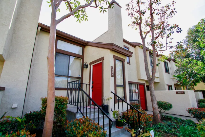 THE HOUSE LOCAED WITH ROOF TOP AND TWO DOORS WITH RED COLOR AND THE STEPS ALSO AVAILABLE AT THE PLACE AND THE TREES AND PLANTS ALSO SURROUNDING THERE AT THE MORNING TIME