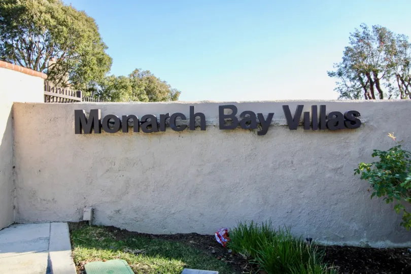 a sunny day in the monarch bay villas with a compound wall that has the name board of the community