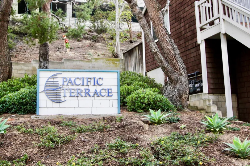 a pleasant day in the pacific terrace with a house that has name board of the community at the side