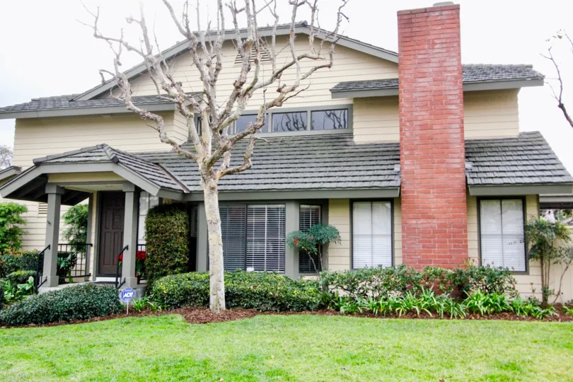 A white and grey house in the Concord Place with beautiful ornamental flowering plants, green grass and shrubs.