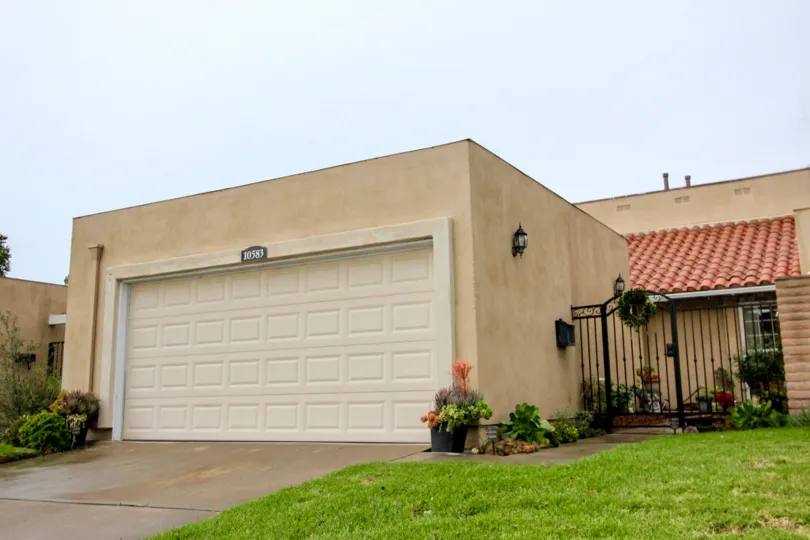 The town home located alone and it looks like sandal color and the front door fully closed and a gate near to the car parking door also closed.