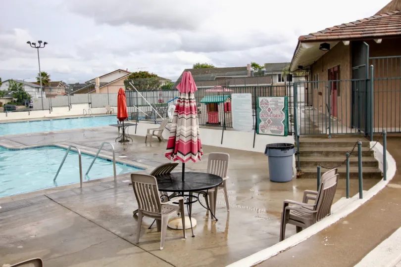 A beautiful swimming pool in the Green Valley Townhomes with buldings, resting chairs and table.