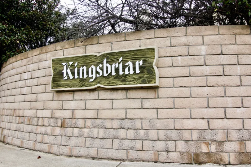 Entrance sign backing made of bricks and the sign is wood and cream lettering showing the community name Kingsbriar.