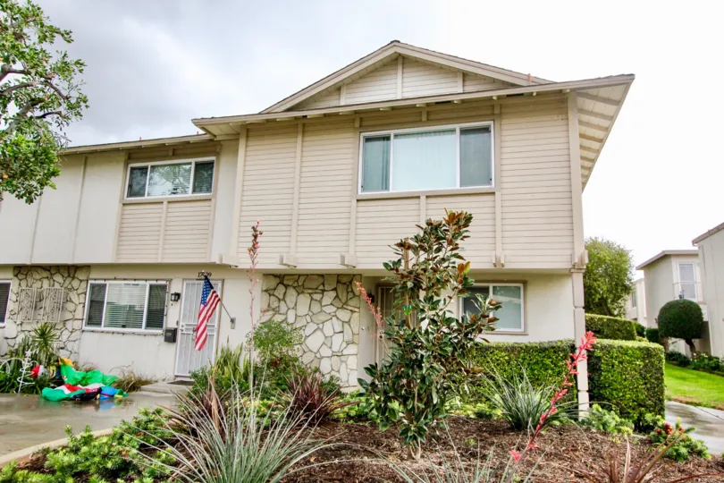 A beautiful grey building in the Paradise Manor with a flag, and glass windows, flowering plants near the house.