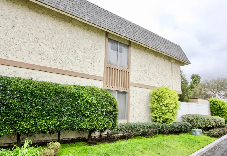 Light tan and dark tan building exterior with bushes lining the wall in Tiburon North community.