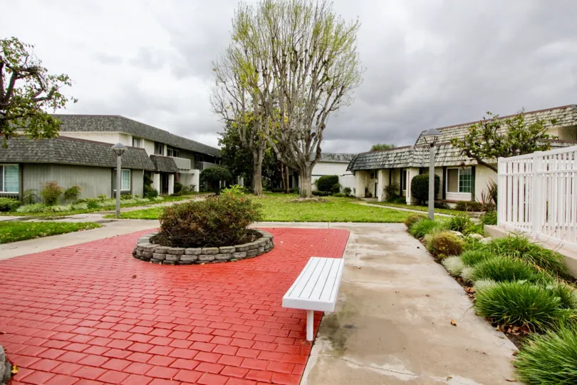 At pathway to Villa's in Tiburon North, has seating benches with bushes, lawn and tall trees