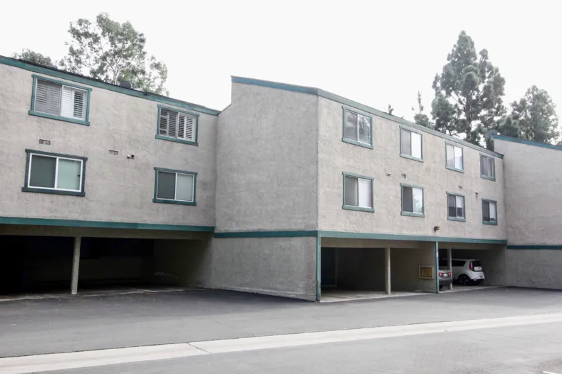 Gray apartment building in Brea Country with parking spaces and green trim.