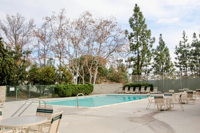 A pool in Case Del Vista with deck chairs and tables on a cloudy day.