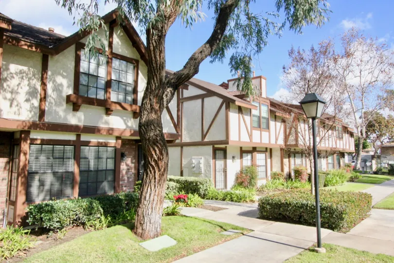 Several homes that are white with wood work all over and bushes and plants in the front in chelsea park estates community in fullerton, california.