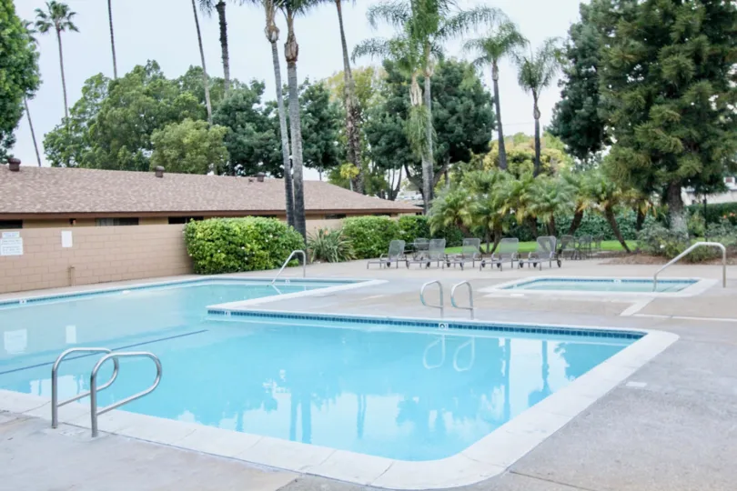 The swimming pool in the Coco Palms with buldings, resting chairs, small ornamental plants, big palm trees and shrubs.
