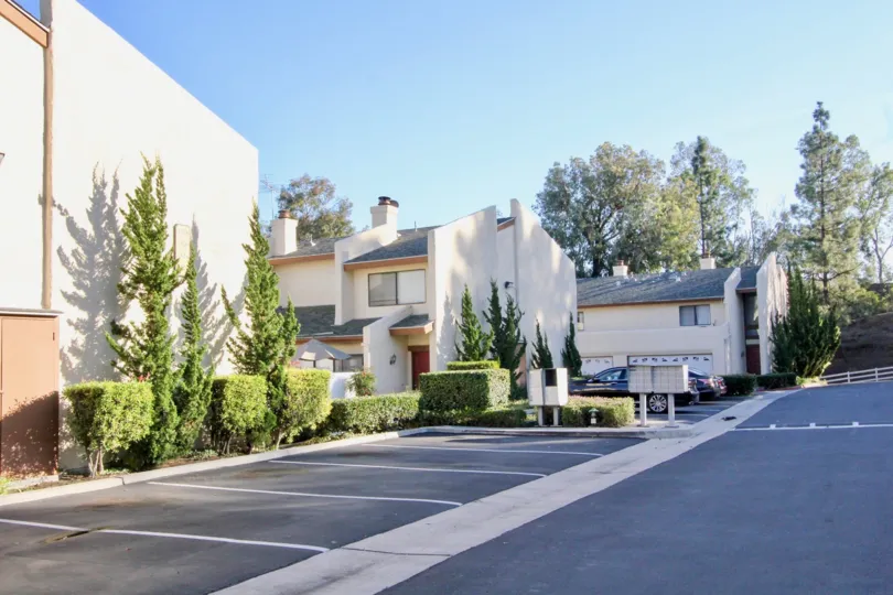 A Country Villas parking lot with trimmed bushes and trees on a sunny day.