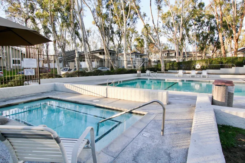 A gated pool and hot tub of Coyote Hills Bluffs with trees and bushes.