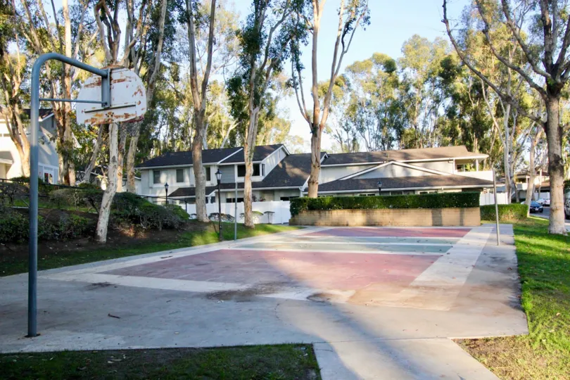 A community basketball court in the Coyote Hills Bluffs neighborhood of Fullerton, California is surrounded by trees and houses.