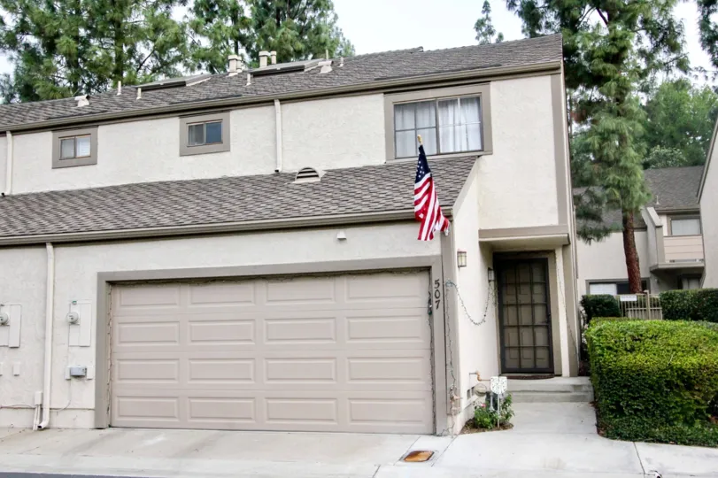 A white two story duplex in Hidden Lakes with a flag on a cloudy day.