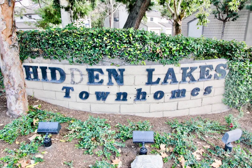 A sign for the Hidden Lakes community with lamps and ivy around it.