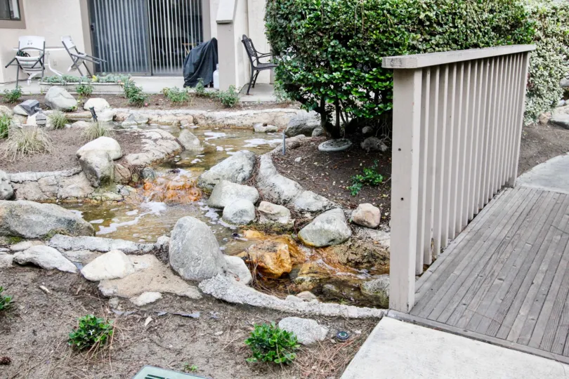 A stream in the Hidden Lakes community with a bridge over it with rock.