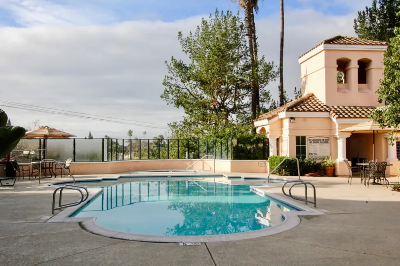 The swimming pool with dining table at the outdoor and a house located near with this pool at the morning sunshine time.