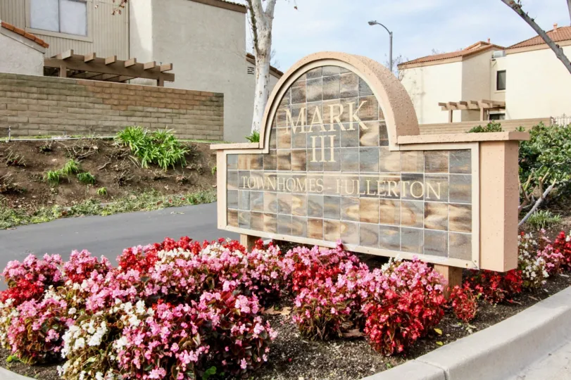 Stone sign to the Mark III Townhomes with flowers on a cloudy day.