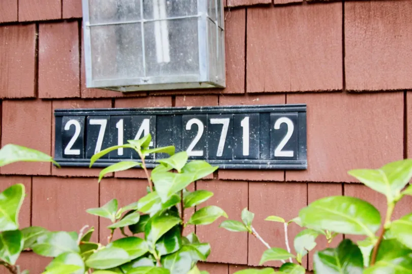 Quail Ridge blue street number with red shingles and plants below.