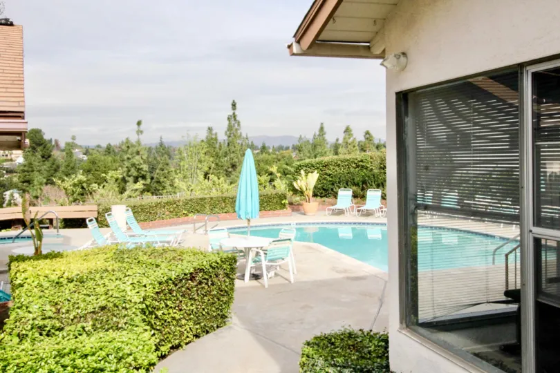 The house with a pool and a dining table also available at the outdoor of the house and a small garden also located near to the pool at the sunshine time.