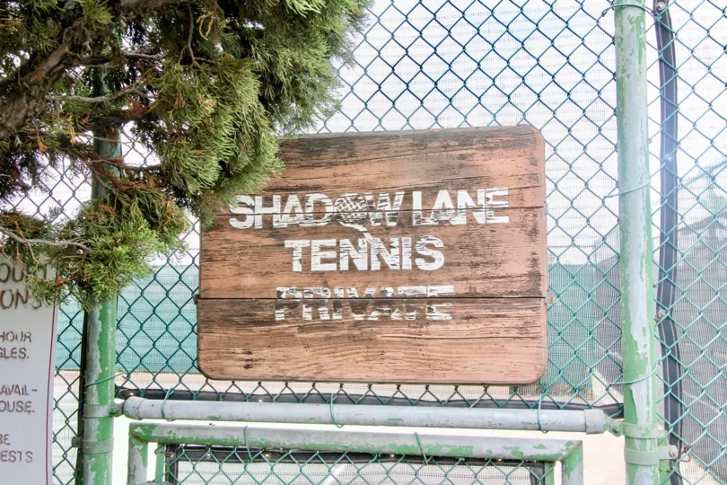 A wooden sign sits against a metal fence at Shadow Lane in Fullerton CA
