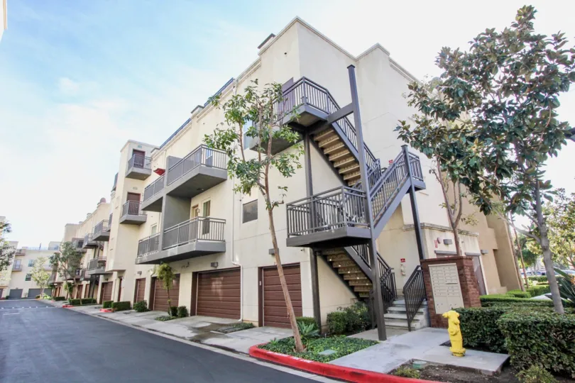 Three story Soco Walk apartments with a staircase and garage on a sunny day.