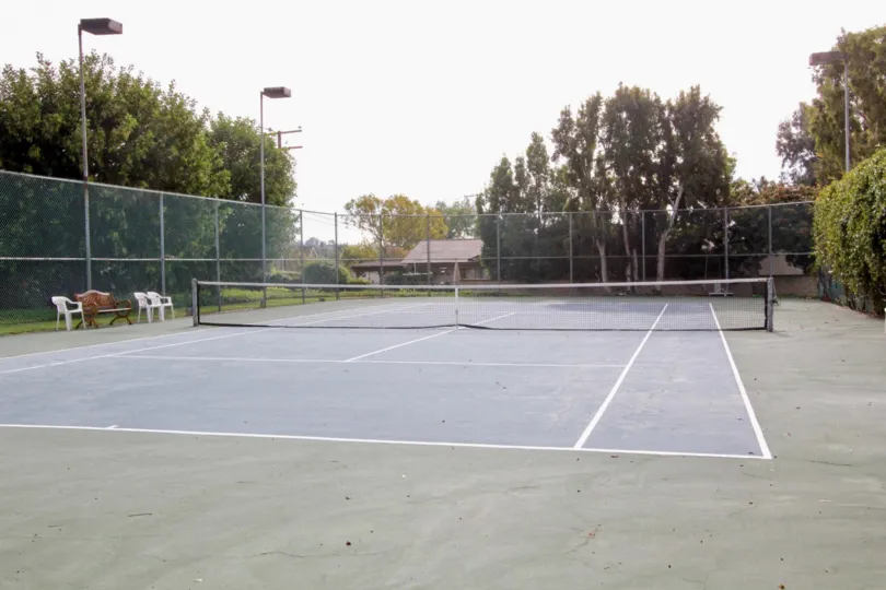 A fenced in tennis court of Stone Pipe with a net a chairs.