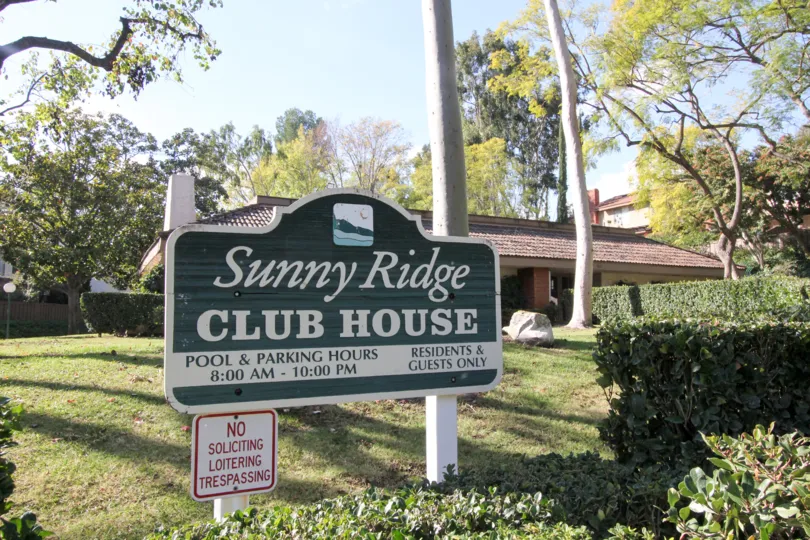 Sunny Ridge Club House sign with pool and parking hours on a sunny day.