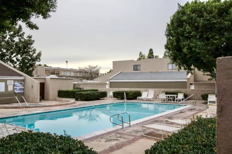 Seating chair, tables and trees are present near the swimming pool in The Arbor