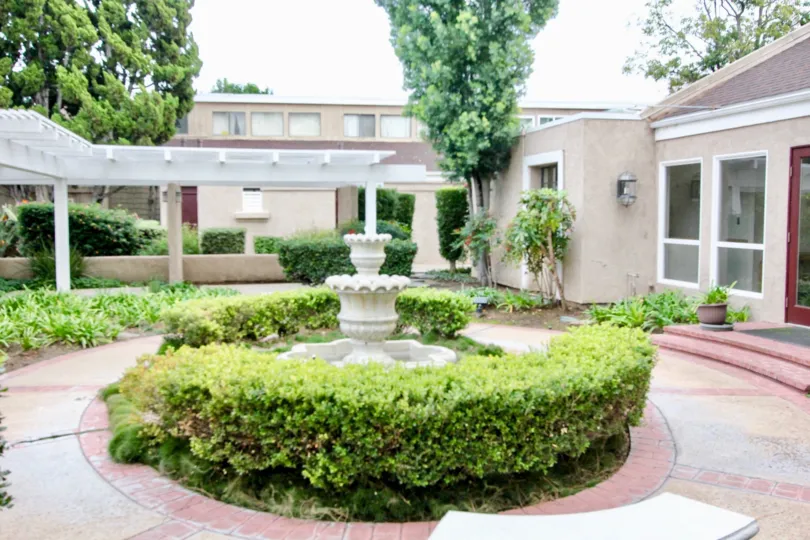 Courtyard in The Arbor with a fountain and bushes on a cloudy day.