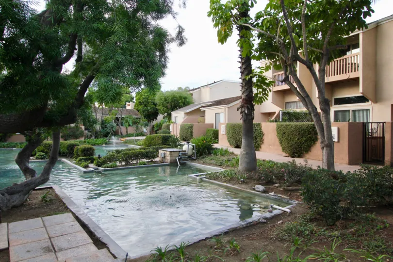 Front to villa in Water Gardens has swimming pool which is full of water with tall trees and palnts