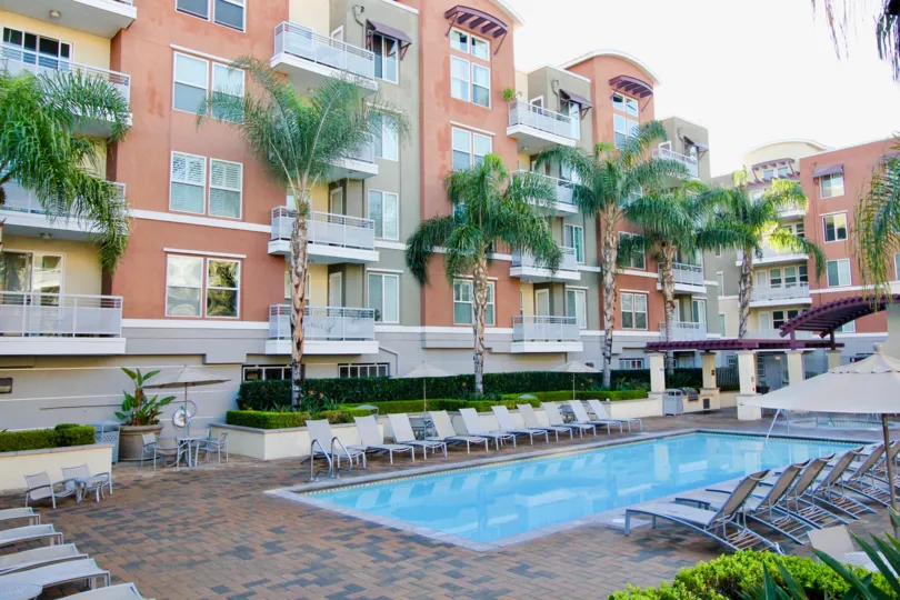 A large swimming pool surrounded by lawn chairs sitting below tall residential buildings at Chapman Commons in Garden Grove CA