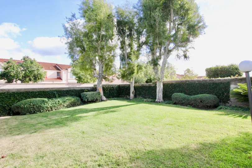 A small play ground and it have three trees placed in corners, it consists trimmed green grass.