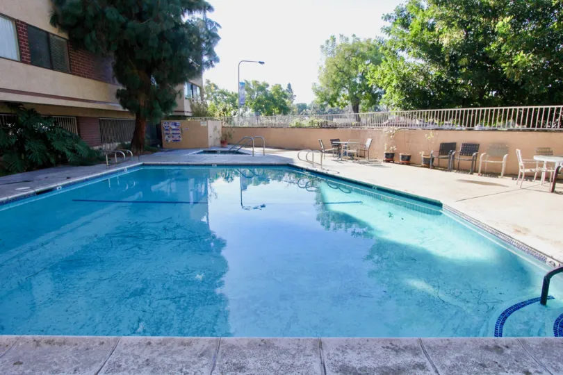 THE SWIMMING POOL WITH LOT OF TREES, CHAIRS SURROUNDED THE WALLS ARE SHOWN IN THE CITY GARDEN GROVE