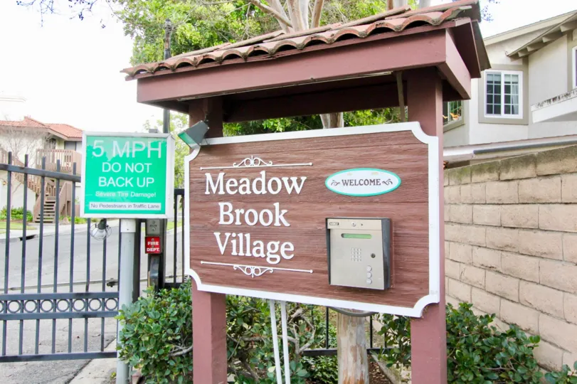 Building at the Meadow Brook Village in Garden Grove with a board and bushes