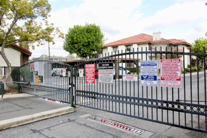 THIS IMAGE REPRESENTS THE FRONT VIEW OF APARTMENTS WHICH SHOWS THE MANY BOARDS ON THE GATE, MANY TREES, PLANTS ARE IN THE CITY OF GARDEN GROVE