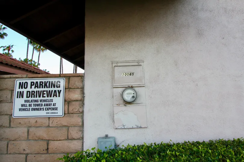 A plaque with hose number and a "No Parking" sign displayed on an exterior wall of a house in Montecito Plaza